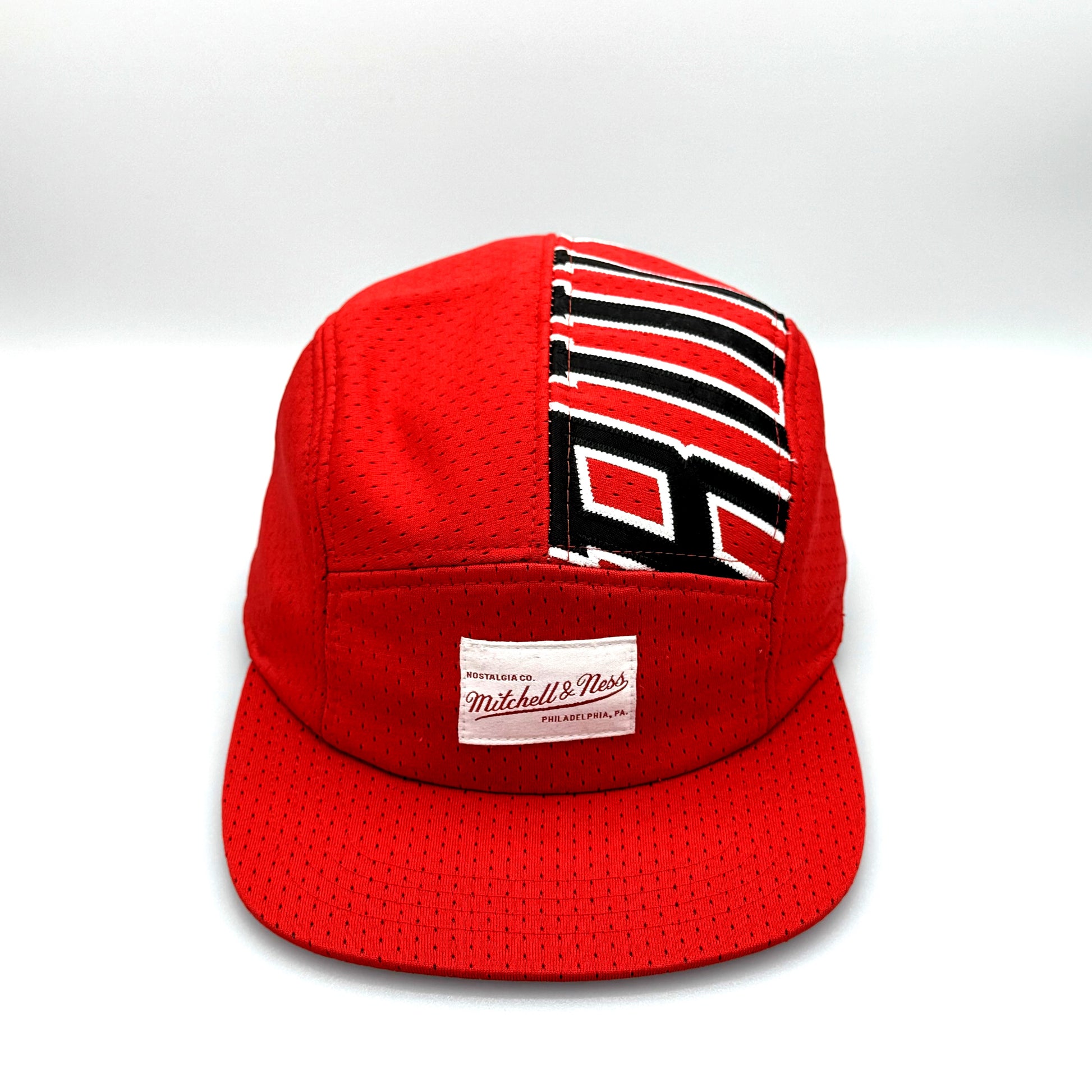 Red and white upcycled MJ jersey made into a 5 Panel Hat, BULLS stitched on the top panel, white background.