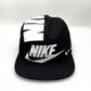 Black and white NIKE shoe box bag upcycled to a 5 Panel Hat, zipper on right side panel, with white background.