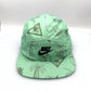 Green NIKE Swim Shorts upcycled into a 5 Panel Hat, black iconic NIKE logo in front, with a white background.