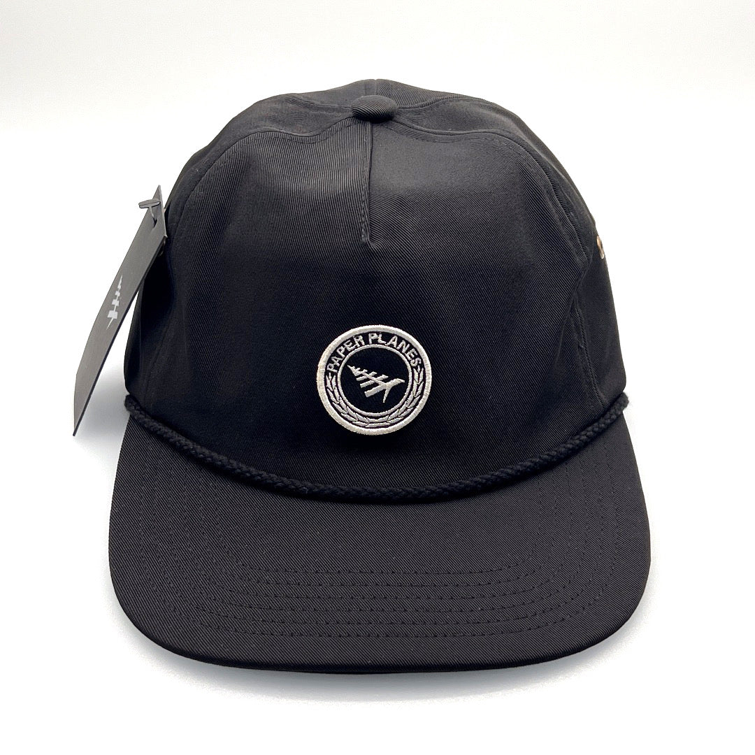Black polyester Paper Planes 5 Panel Hat, embroidered logo on the front, with a white background.