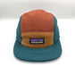 Brown, tan and cyan Patagonia fleece 5 Panel Hat upcycled, iconic logo on the front, with a white background.