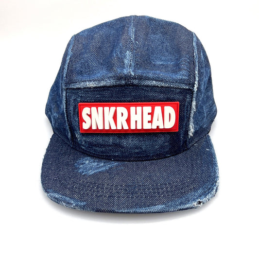 Distressed blue denim SNKRHEAD 5 Panel Hat, rubber logo on the front, with a white background.