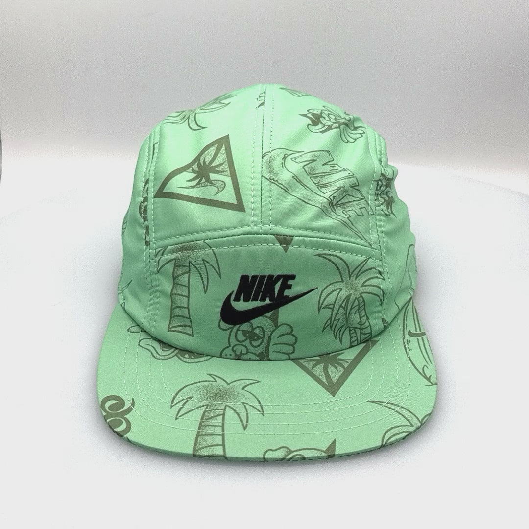 Spinning green NIKE Swim Shorts upcycled into a 5 Panel Hat, black iconic NIKE logo in front, with a white background.