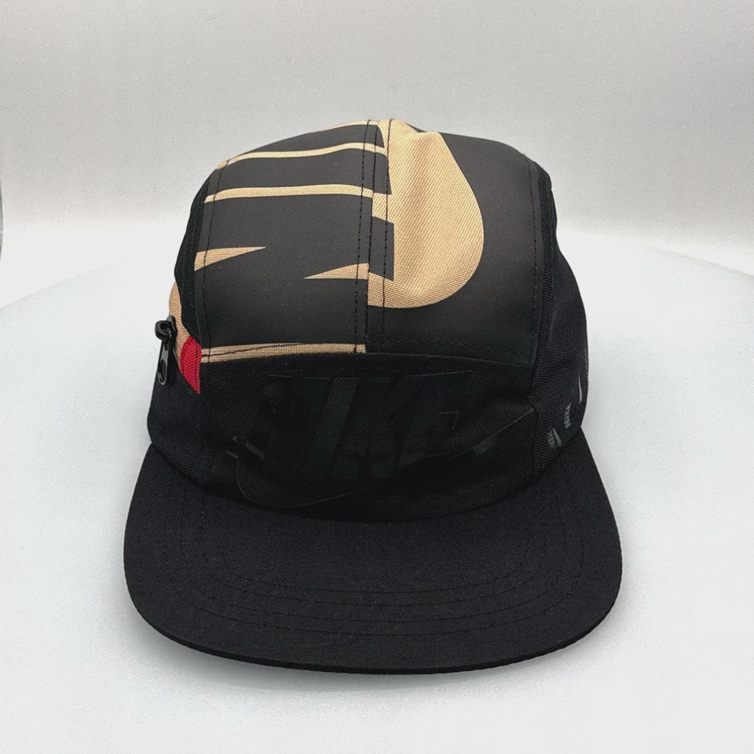 Spinning black and tan NIKE shoe box bag upcycled to a 5 Panel Hat, zipper on right side panel, with white background.