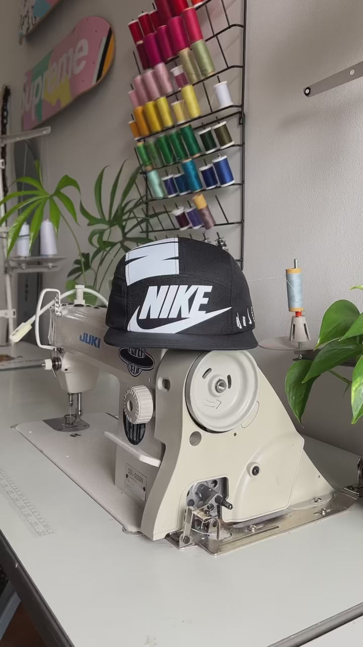 The making of a Black and white NIKE shoe box bag upcycled to a 5 Panel Hat, zipper on right side panel, with white background.