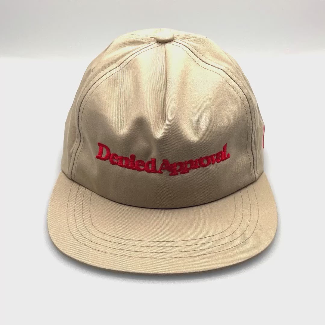 Spinning Khaki Denied Approval 5 Panel Hat with red logo on the front, white background.