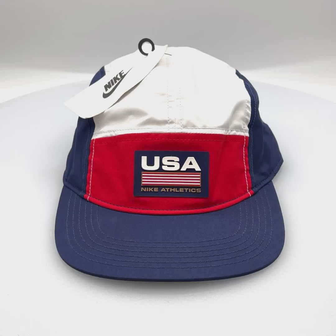 Spinning red, white and blue USA NIKE Athletics 5 Panel Hat, rubber logo on front, with a white bachground.