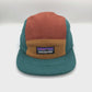 Spinning brown, tan and cyan Patagonia fleece 5 Panel Hat upcycled, iconic logo on the front, with a white background.