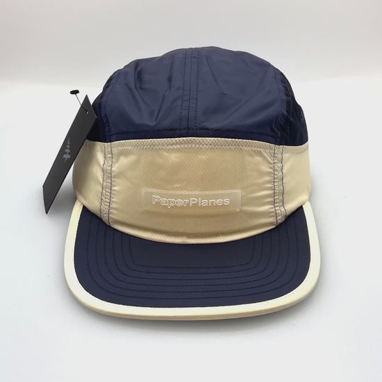 Spinning nylon navy and off white Paper Planes 5 Panel Hat, clear logo on the front, with a white background.