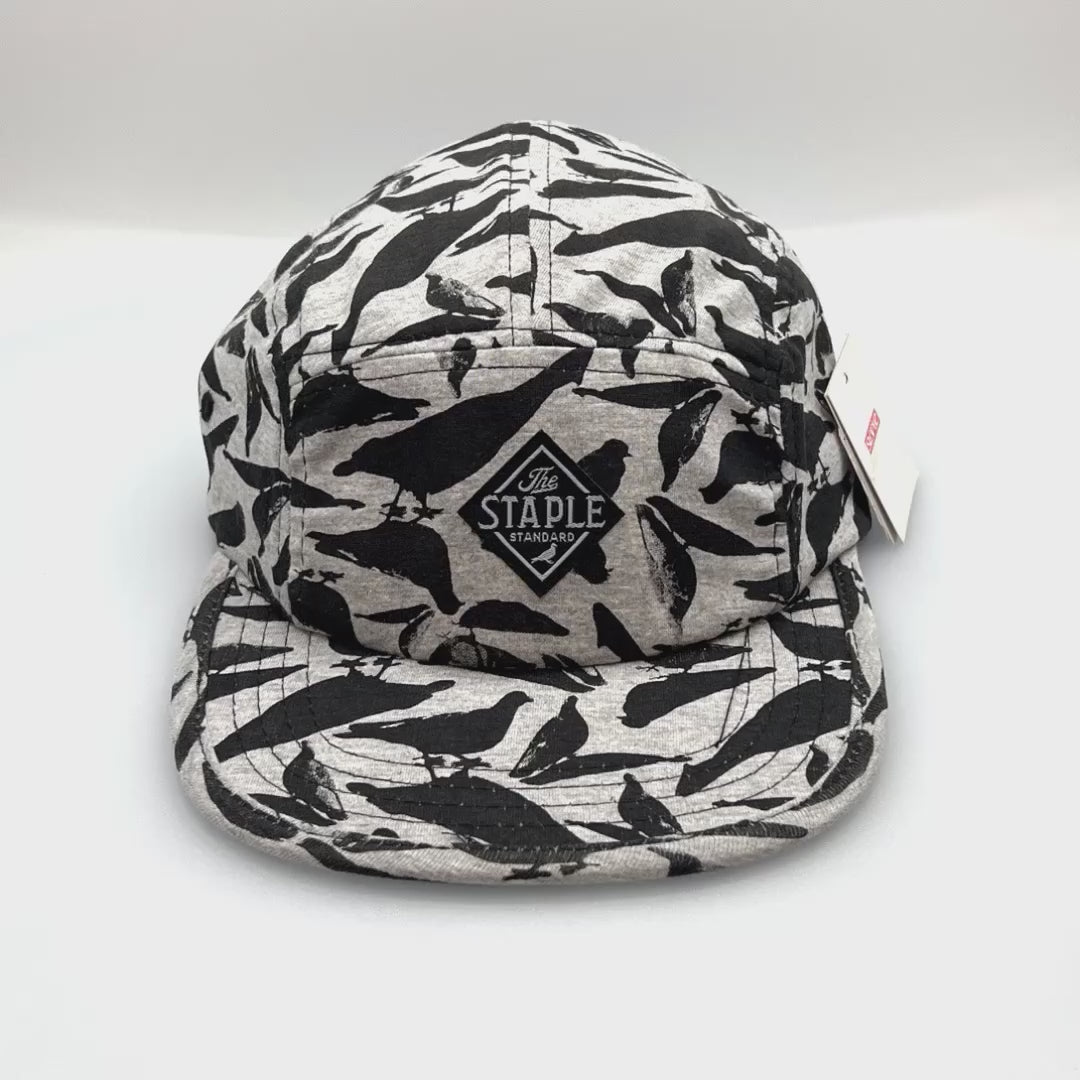 Spinning grey and black Staple Standard Pigeon 5 Panel Hat, with a white background.