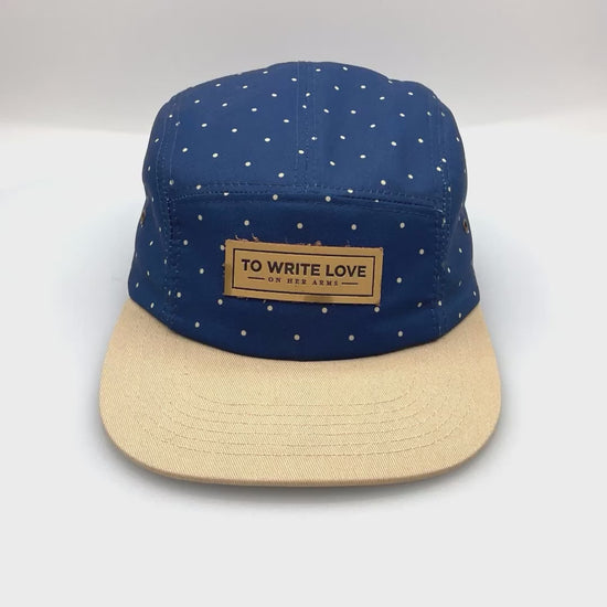 Spinning tan and navy polka dots TWLOHA 5 Panel Hat, leather logo on the front, with a white background.