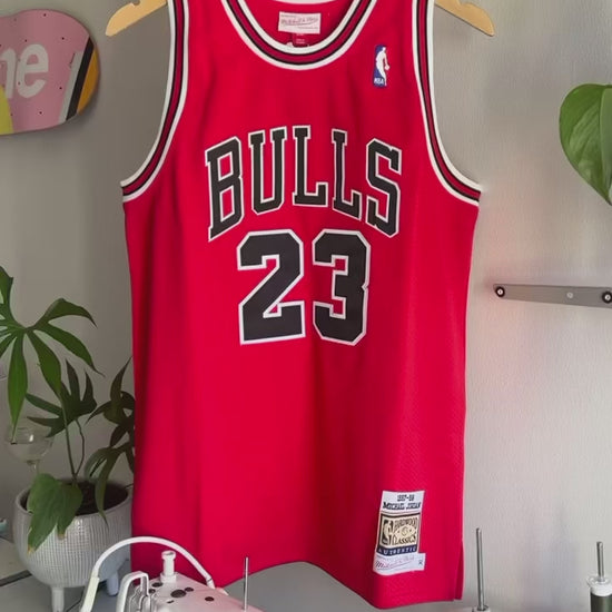 The making of a red and white upcycled MJ jersey made into a 5 Panel Hat, BULLS stitched on the top panel, white background.