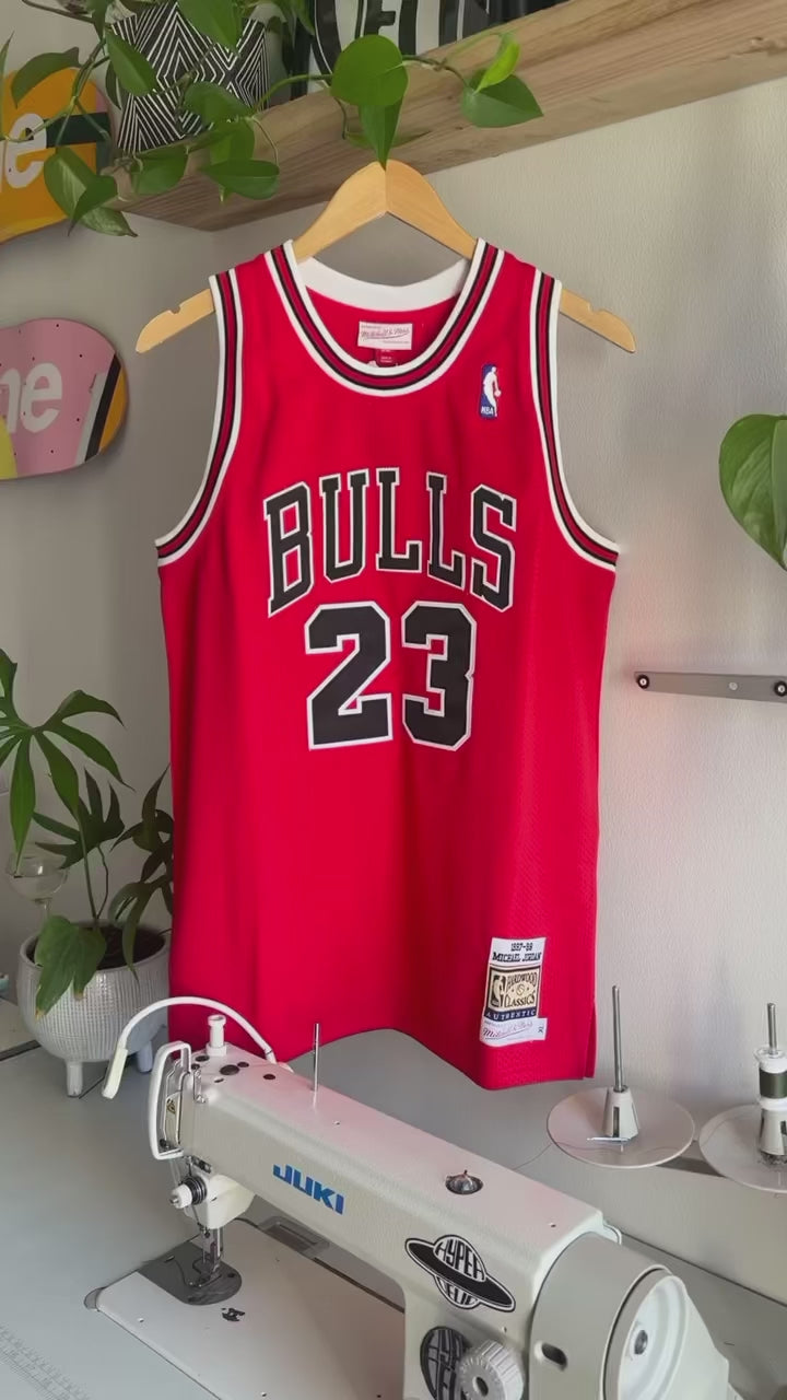 The making of a red and white upcycled MJ jersey made into a 5 Panel Hat, BULLS stitched on the top panel, white background.