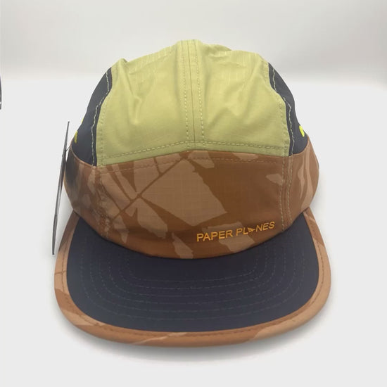 Spinning nylon navy, brown, and olive Paper Planes 5 Panel Hat, orange Paper Planes logo on the front, with a white background.