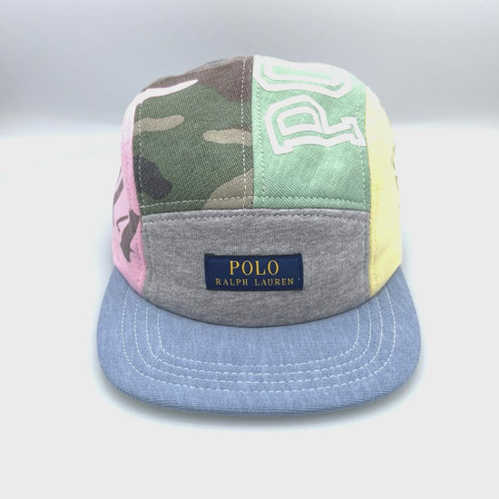 Spinning camo, blue, green, grey and pink patchwork Polo 5 Panel Hat upcycled, iconic Polo RL logo on the front, with a white background.